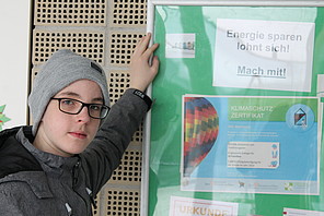 Schüler mit Energiespar-Plakat Schüler steht vor einer Schauwand mit der Aufschrift "Energie sparen" lohnt sich.