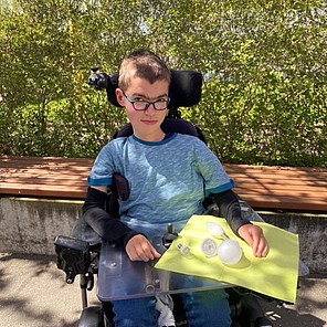 Paul vor der Berufsbildenden Schule am BBW Chemnitz Vor Paul, der in einem elektrischen Rollstuhl sitzt, liegen auf seinem dazugehörigen Plexiglas-Pult LED-Lampen in unterschiedlichen Arten und Größen. Zum besseren Kontrast liegen die weißen Lampen auf einer hellgrünen Serviette.